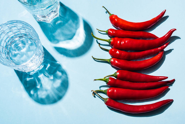 Top view of fresh chili peppers beside glasses of water on blue background - Photo, Image