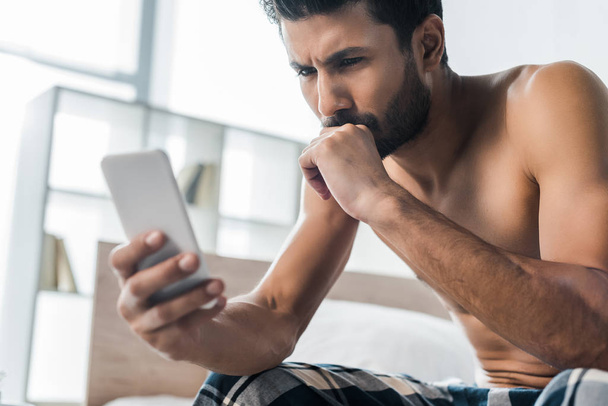 foco seletivo de homem bi-racial pensativo e sexy usando smartphone de manhã
  - Foto, Imagem