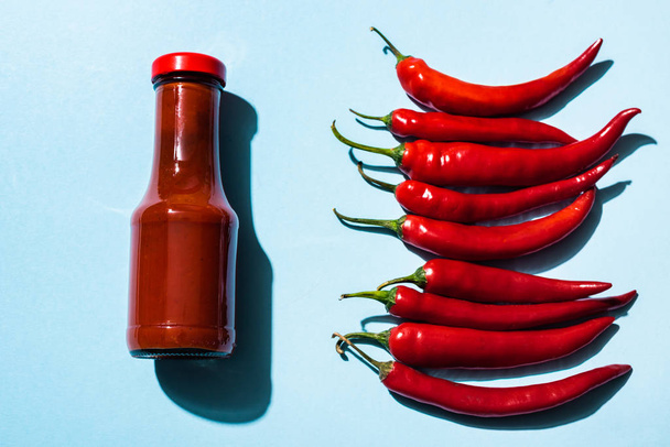 Top view of chili sauce and ripe chili peppers on blue surface - Foto, Imagem