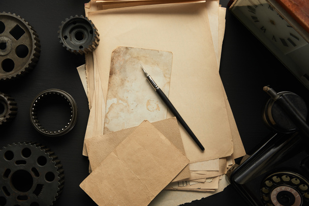 Ansicht von alternden Zahnrädern und Altpapier mit Füllfederhalter auf schwarzer Oberfläche - Foto, Bild