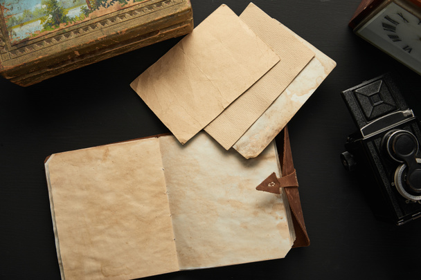 bovenaanzicht van vintage camera, papier, schilderen, klok en notitieblok op zwarte achtergrond - Foto, afbeelding