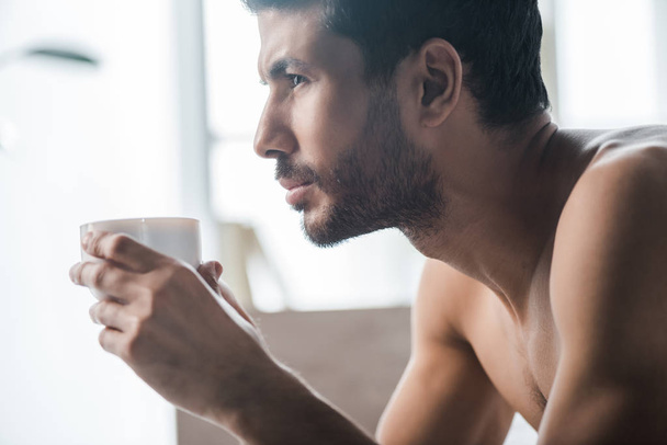 side view of handsome bi-racial man holding cup of coffee in morning  - Fotó, kép