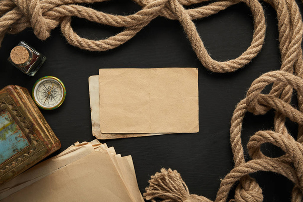 top view of vintage paper, rope, compass and painting on black background - Fotoğraf, Görsel