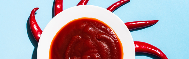 Вид сверху перца чили вокруг тарелки с томатным соусом на голубой поверхности, панорамный снимок
 - Фото, изображение
