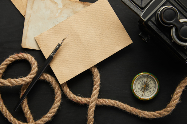 top view of vintage camera, paper, rope, fountain pen, compass on black background - Valokuva, kuva