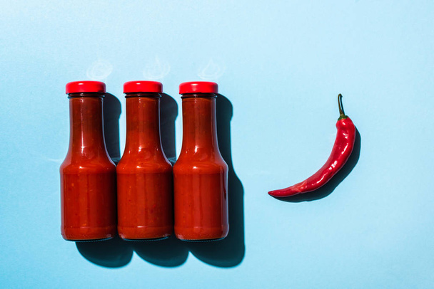 Top view of tasty chili sauce with chili pepper on blue surface - 写真・画像