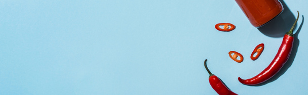 Вид зверху гострий перець чилі з кетчупом у пляшці на синій поверхні, панорамний знімок
 - Фото, зображення