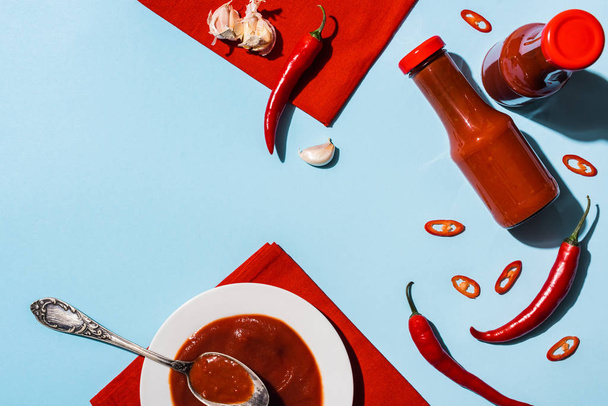 Top view of homemade chili sauce with garlic and chili pepper on blue surface - Foto, afbeelding