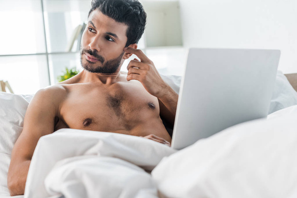 handsome and pensive bi-racial man with laptop looking away in morning  - Fotó, kép