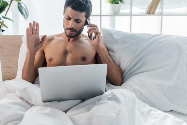 handsome bi-racial man with laptop talking on smartphone in morning  - Photo, Image