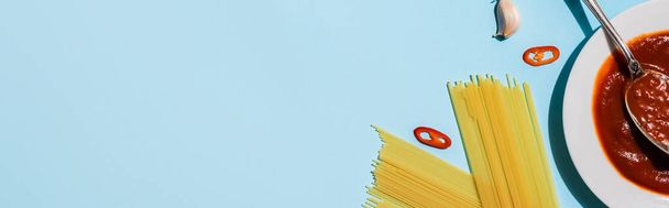 Top näkymä kotitekoinen ketsuppi vieressä raaka spagetti sinisellä pohjalla, panoraama laukaus
 - Valokuva, kuva