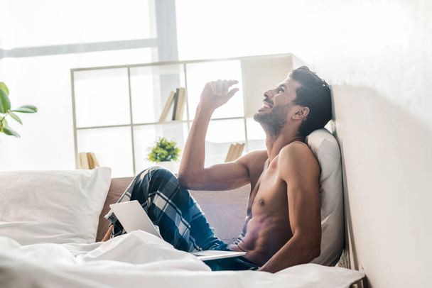 side view of handsome and smiling bi-racial man with laptop in morning  - Photo, Image