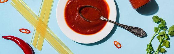 Vista superior de molho de pimenta com espaguete, pimentão e vegetação no fundo azul, tiro panorâmico
 - Foto, Imagem