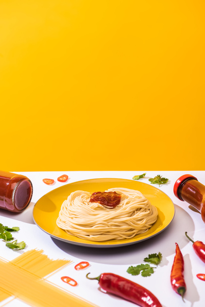Delicious spaghetti with ketchup, cilantro and chili peppers on white surface on yellow background - Photo, Image