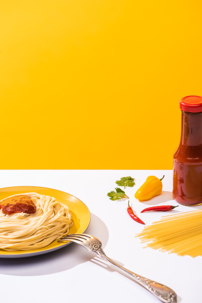 Delicious spaghetti with ketchup and peppers on white surface on yellow background - 写真・画像