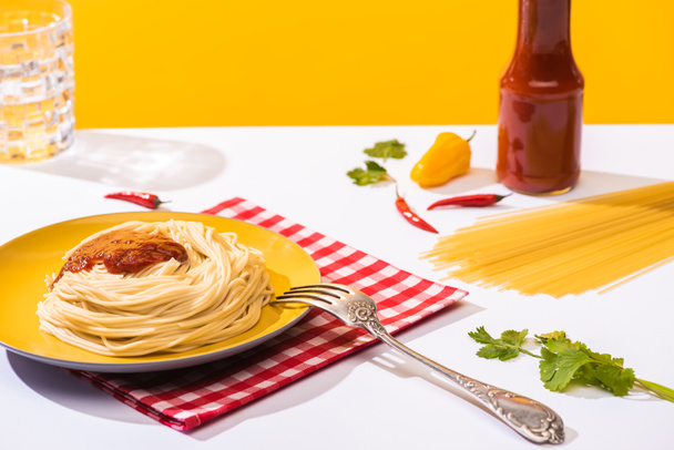 Focus selettivo di spaghetti fatti in casa con ketchup, coriandolo e peperoni su superficie bianca su fondo giallo
 - Foto, immagini