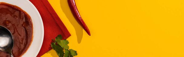 Widok z góry sosu pomidorowego w talerzu z kolendrą i papryką chili na żółtym tle, zdjęcie panoramiczne - Zdjęcie, obraz