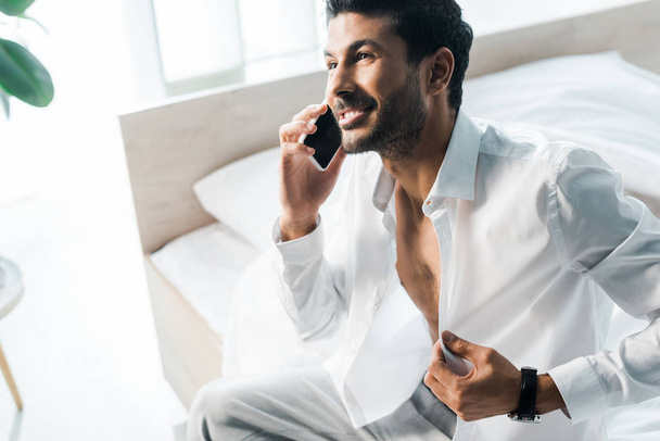 high angle view of smiling and handsome bi-racial man talking on smartphone in morning  - 写真・画像