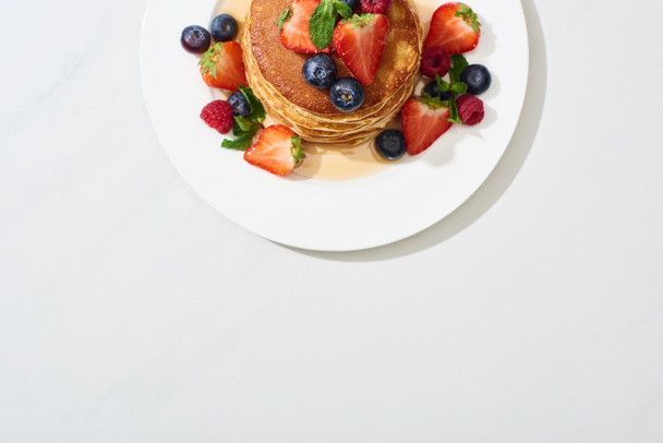 top view of delicious pancakes with honey, blueberries and strawberries on marble white surface - Foto, imagen