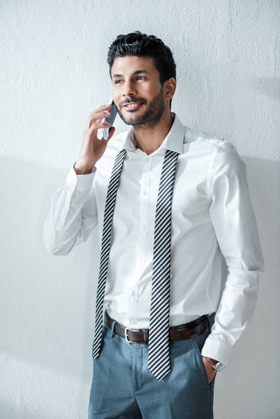 pohledný a usmívající se bi-rasový podnikatel mluví na smartphone v dopoledních hodinách doma  - Fotografie, Obrázek