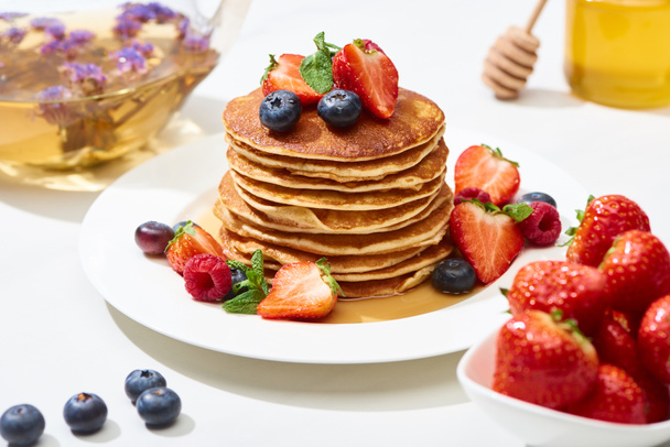 selective focus of delicious pancakes with honey, blueberries and strawberries on plate on white surface - Foto, Bild