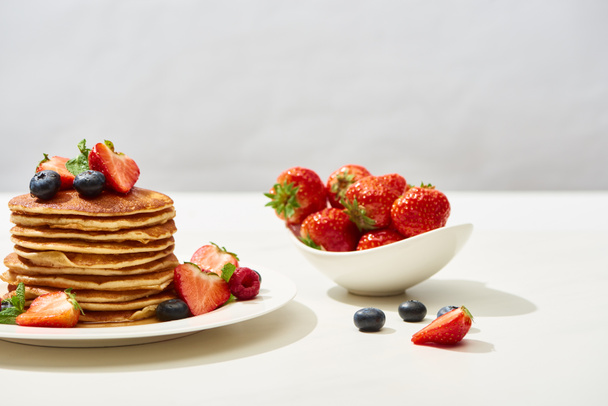 delicious pancakes with blueberries and strawberries on plate on white surface isolated on grey - Photo, Image