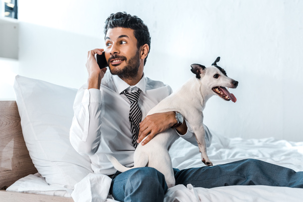 bi-raciale zakenman houdt Jack Russell Terrier en praten op de smartphone in de ochtend  - Foto, afbeelding