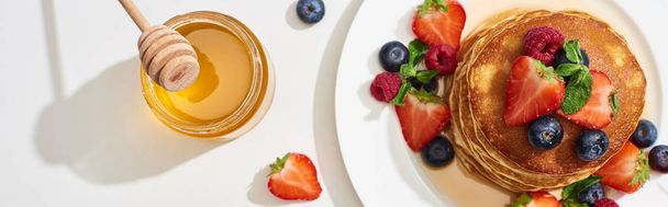 vista dall'alto di deliziose frittelle con miele, mirtilli e fragole sul piatto su superficie bianca di marmo, colpo panoramico
 - Foto, immagini