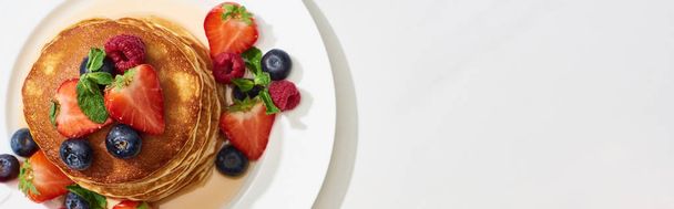 top view of delicious pancakes with honey, blueberries and strawberries on plate on marble white surface, panoramic shot - Fotoğraf, Görsel