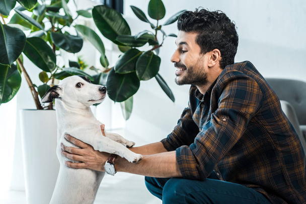 side view of handsome and smiling bi-racial man holding jack russell terrier - Foto, Bild