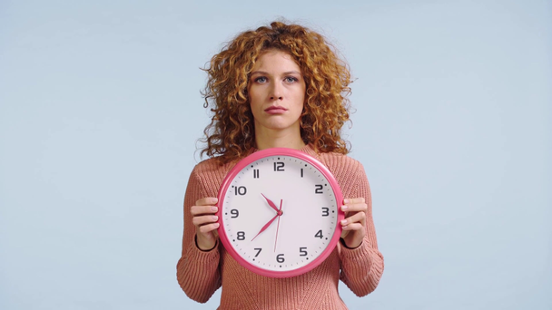 Unzufriedene Frau versteckt Gesicht hinter Uhr auf blauem Grund - Filmmaterial, Video