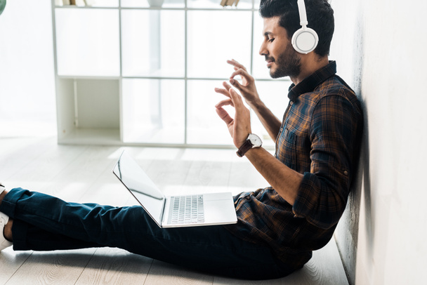 side view of handsome and smiling bi-racial man with laptop listening music  - Fotoğraf, Görsel