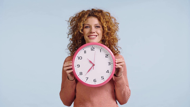 cheerful woman looking out from behind clock isolated on grey - Footage, Video
