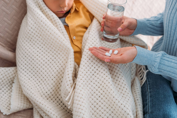 cropped view of woman holding pills and glass of water near ill son - Photo, Image