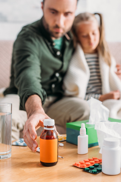 selective focus of man taking cough syrup while sitting near diseased daughter - Photo, Image