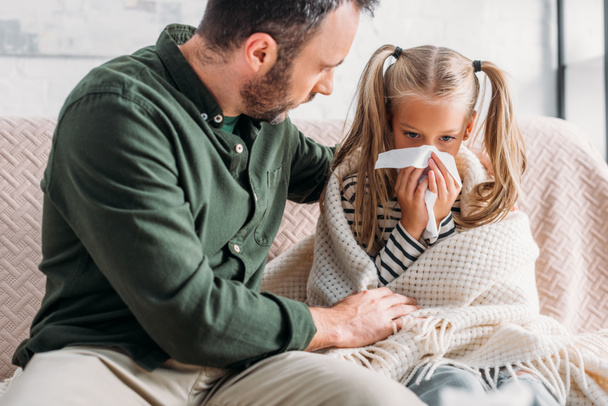 attentive father embracing sick daughter sneezing in napkin - Фото, зображення