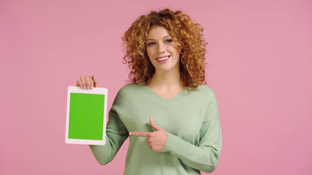 χαμογελαστή γυναίκα που δείχνει ψηφιακό δισκίο με πράσινη οθόνη απομονωμένη σε ροζ - Πλάνα, βίντεο