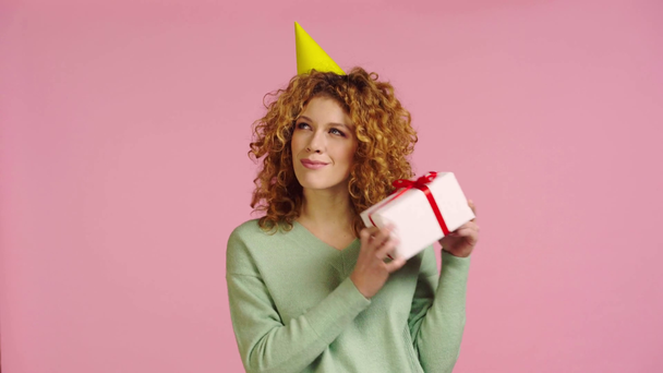 woman shaking gift box and showing shrug gesture isolated on pink - Footage, Video