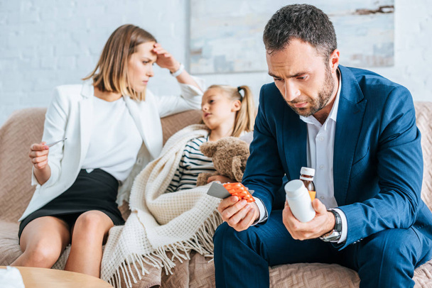 worried father holding medicines and mother sitting near diseased daughter  - Photo, Image