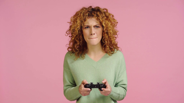 KYIV, UKRAINE - NOVEMBER 27, 2019: cheerful woman playing video game isolated on pink - Кадри, відео
