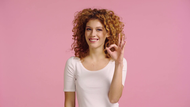 šťastná žena ukazuje ok gesto a přikyvování izolované na růžové - Záběry, video