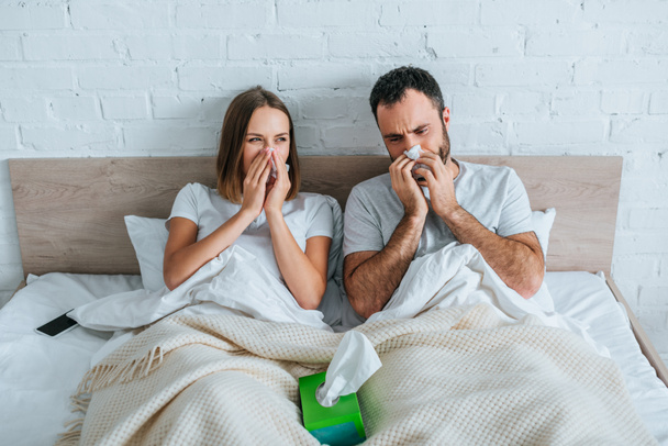 diseased husband and wife sneezing while lying in bed together - Foto, imagen