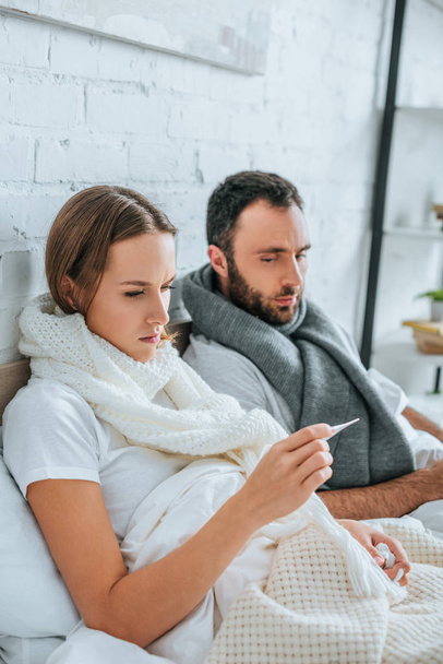 sick woman looking at thermometer near diseased husband - Photo, image