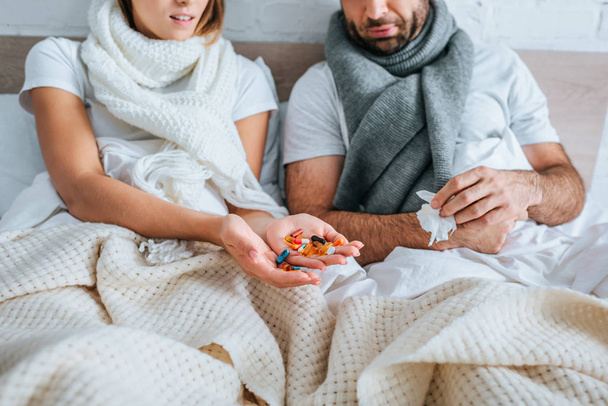 bijgesneden beeld van zieke vrouw met handvol pillen terwijl ze in bed in de buurt van zieke man - Foto, afbeelding