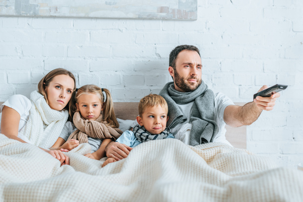 άρρωστη οικογένεια ξαπλωμένη στο κρεβάτι και βλέποντας τηλεόραση μαζί - Φωτογραφία, εικόνα