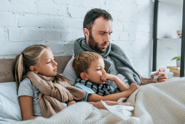 upset father looking at thermometer while lying in bed with diseased children - Фото, зображення