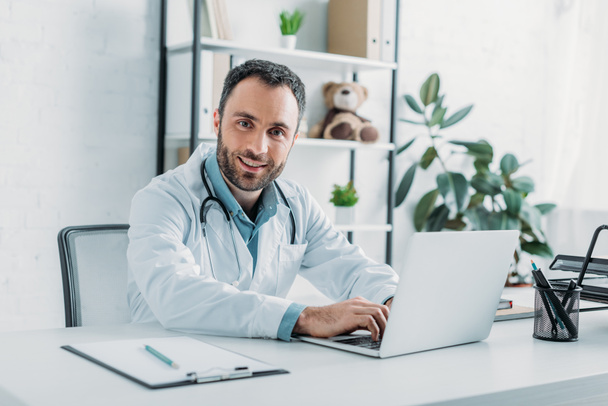 smiling doctor looking at camera while using laptop - Photo, Image