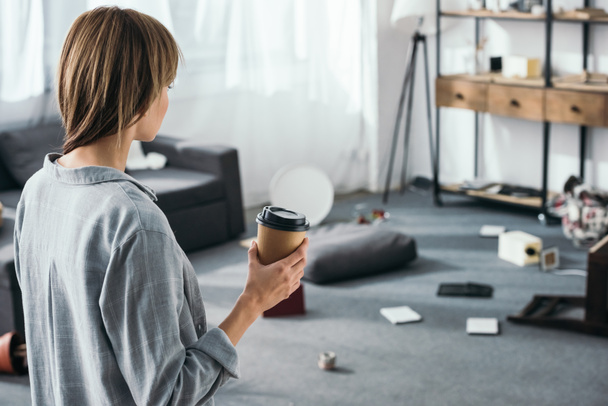 женщина держит бумажную чашку и смотрит на ограбленную квартиру
  - Фото, изображение