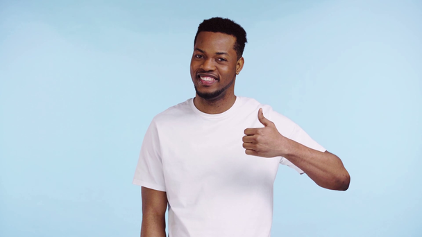 šťastný afroamerický muž ukazující na palec izolovaný na modrém - Záběry, video