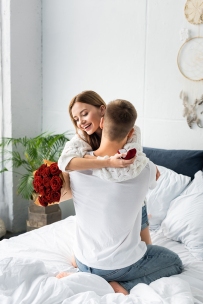 back view of of man with bouquet and smiling woman hugging him with box  - Фото, зображення